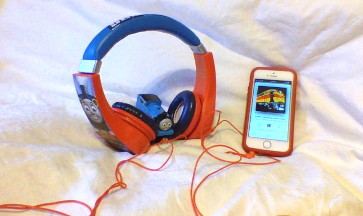An Experiential Learning Depot created photo of a Thomas the Train toy listening to a podcast from a cell phone, with Thomas the Train head phones.